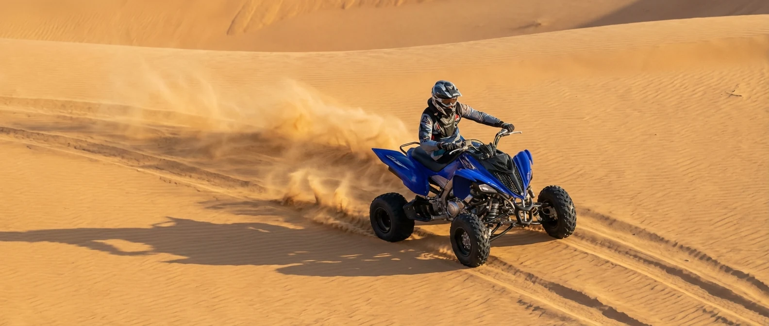 Blue and black manual 700 cc sport quad bike carving across open Dubai dunes